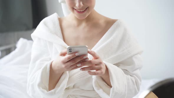 Healthy Relaxed Woman Sits Using Smartphone Having Rest on Bed After Bathroom