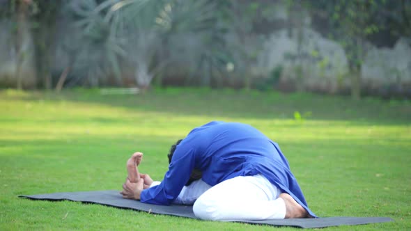 Indian man doing Folded leg forward bend yoga or Triang Mukha Eka Pada Paschimottanasana alt