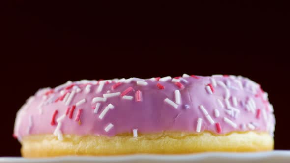 Delicious pink donut on a plate rotates on a black background. alt