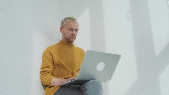 Portrait of a Young European Male Freelancer Sitting at the Balcony with the Laptop Multitasking alt