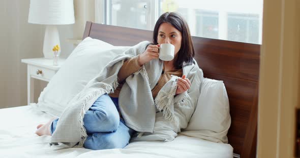 Thoughtful woman wrapped in blanket having coffee 4k alt