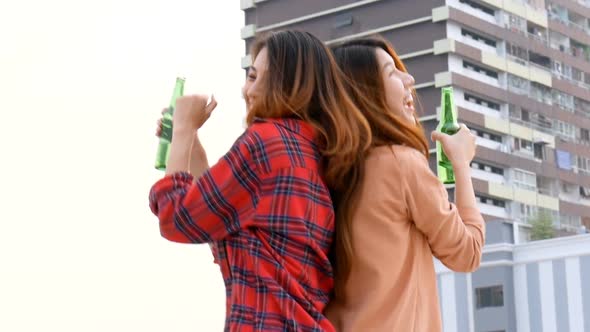 Young Asian woman lesbian couple dancing and clinking bottles of beer party on the rooftop.