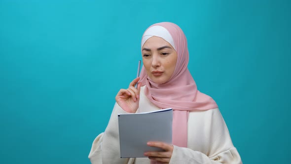 Happy Beautiful Young Muslim Woman in Hijab Making Notes in Paper Notebook Writing Creative Idea