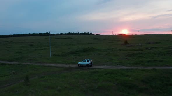 Aerial View of a Car Driving in Nature on a Field at Sunset alt