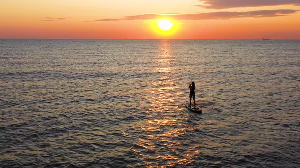 Young woman silhouette on a stand up paddle board. Sunset light in the water. alt