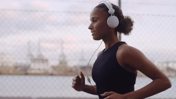 Young Woman In Sportswear And Headphones Jogging Along Harbour alt