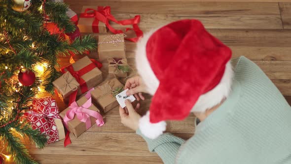 Writing Greeting Card for Christmas Presents Female Red Hat Under Fir Tree Gifts alt
