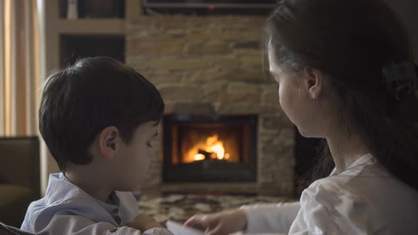 Mother and son at the fireplace where the fire is burning learn poems by heart alt