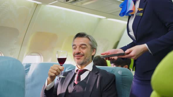 Caucasian flight attendant serving red wine to Businessman passenger in business class on airplane. alt