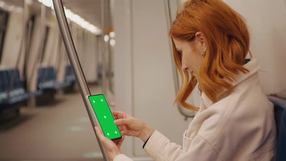 Tourist woman sitting in metro and scrolls the green screen phone on the train. alt