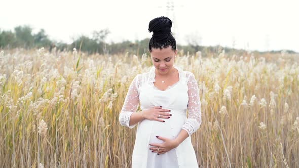 Young pretty pregnant woman posing on nature background. Expectant mother waiting for a baby.  alt