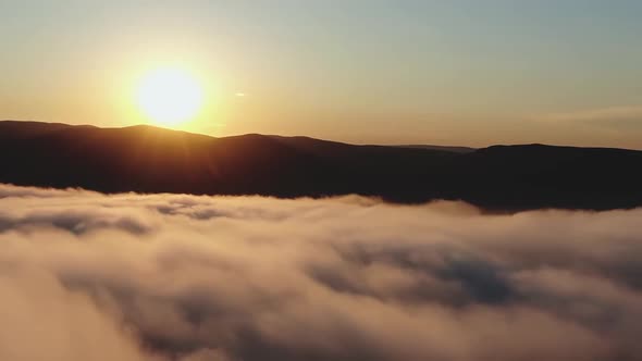 Aerial Drone Footage of Pink Mist Swirls at the Foot of a Mountain Range at Sunset alt