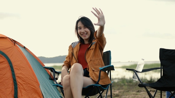 A beautiful Asian woman feels shy when her boyfriend taking a photo in front of the tent.