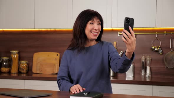 Smiling Woman Greets Talking Online Video Call Webcam Smartphone in Home Kitchen alt