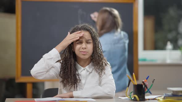 Portrait of Sad Exhausted African American Schoolgirl Falling Asleep Sitting at Desk in Classroom alt
