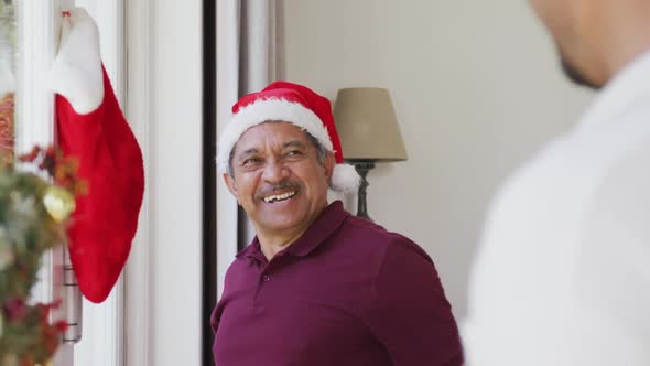 Cheerful senior man hanging christmas sock on window and patting son at home alt