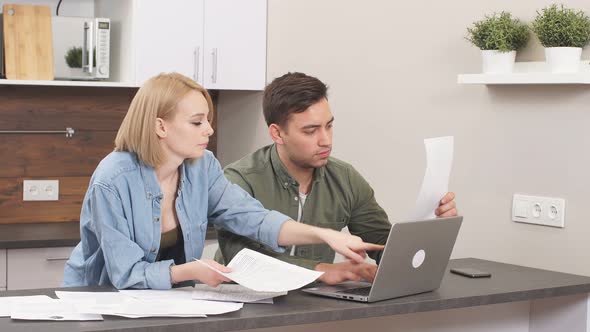 Caucasian Young Couple Reading and Analyzing Bills Sitting at Table alt