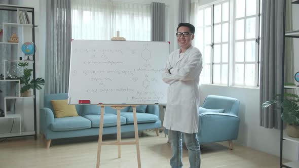 Asian Male Teacher With Glasses Crossing Arms And Smiling To Camera While Teaching Chemist At Home alt