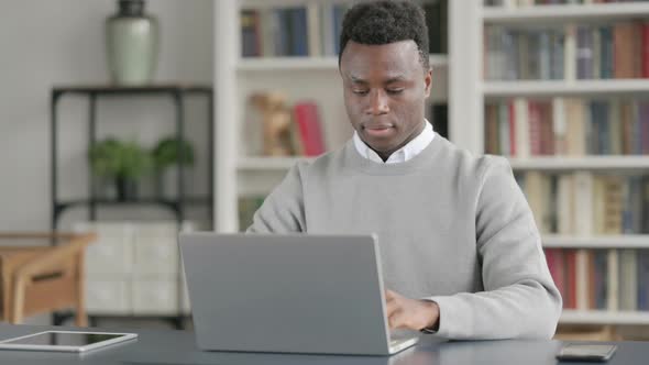 African Man Showing Thumbs Up Sign While Using Laptop at Work alt