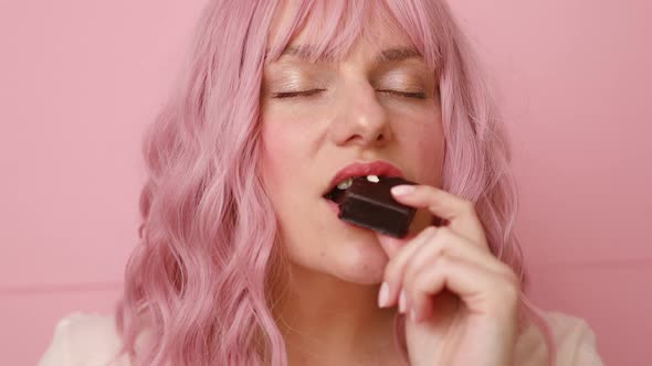 Portrait of Beautiful Young Woman Biting in a Pieace of Chocolate Waffle Candy Isolated Over Pink