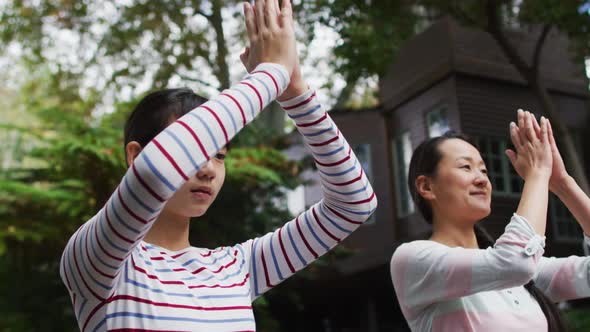 Happy asian mother exercising in garden with daughter, practicing tai chi together alt