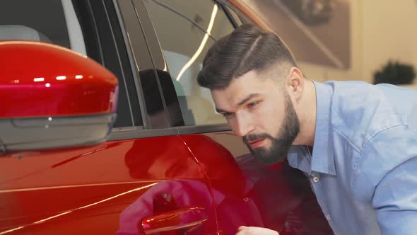 Cheerful Man Smiling to the Camera While Examining Car at the Dealership alt