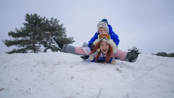Outdoor Activities Joyful Mother with Male Child Have Fun Sledding Down Snowy Hill in Forest on