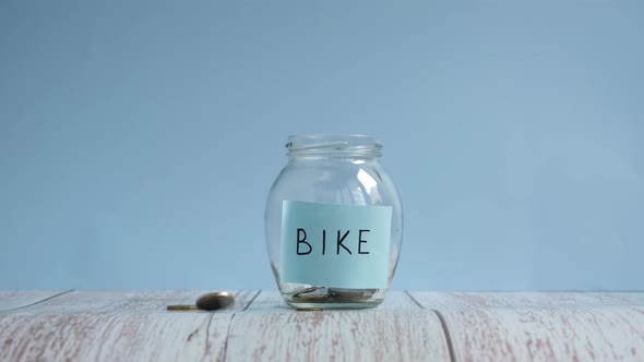 Saving money for bike. Throwing coins into glass jar with inscription bike alt