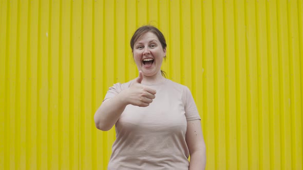 Positive Overweight Woman Showing Class Sign Thumbs Up Against Yellow Wall alt