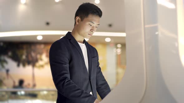 Young Asian Man in Jacket and Shirt Searching for Info in Interactive Wayfinding Kiosk