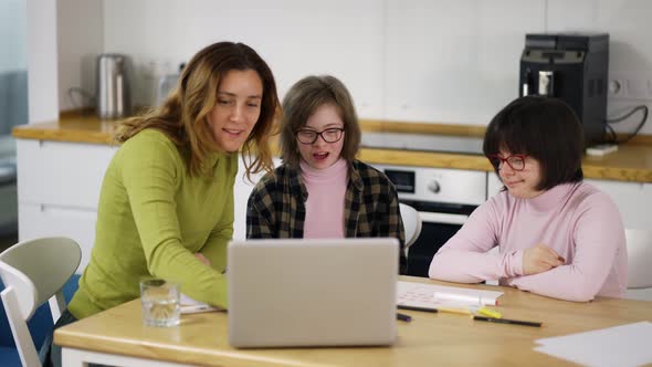 Teacher Teaches Young Girls with Down Syndrome to Use a Laptop at the Kitchen alt