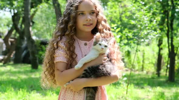 Little Girl with Curly Hair Holding a Little Cat in Her Arms alt