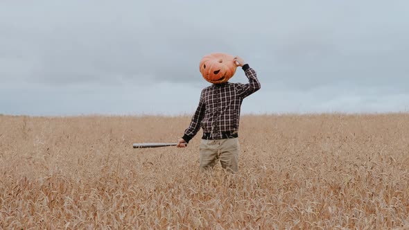 A Man with a Large Pumpkin on His Head and a Bat in His Hands Poses for the Camera Standing in a