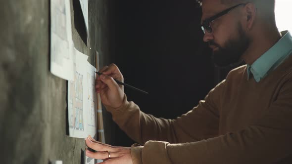 Designer Works in Loft Office and Makes Notes on the Drawings on Wall