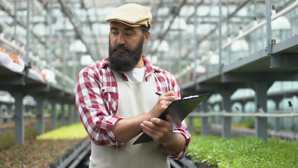 Busy Farmer Writing Research Paper in Greenhouse, Studying Breeding Technologies