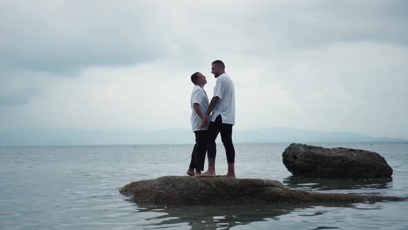 Flirting Gay Couple Having a Romantic Kiss Standing on a Rock Sticking Out of Seawater alt