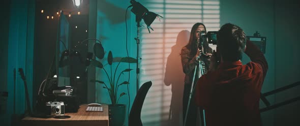 Filmmaker is setting up the camera for the video and his model is moving on the background alt