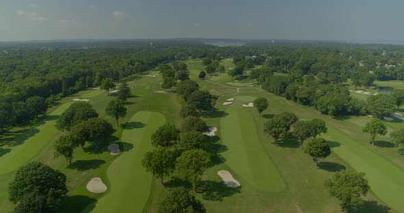 Flying Over a Golf Course with Trees Near a Forest on a Sunny Day alt