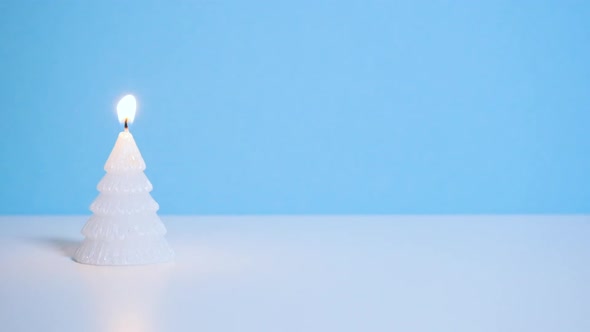 White Christmas Tree Wax Candle Burning on Blue Background