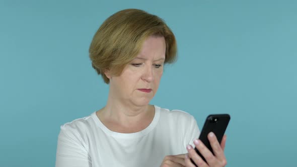 Amazed Old Woman Excited While Using Smartphone Isolated on Blue Background alt
