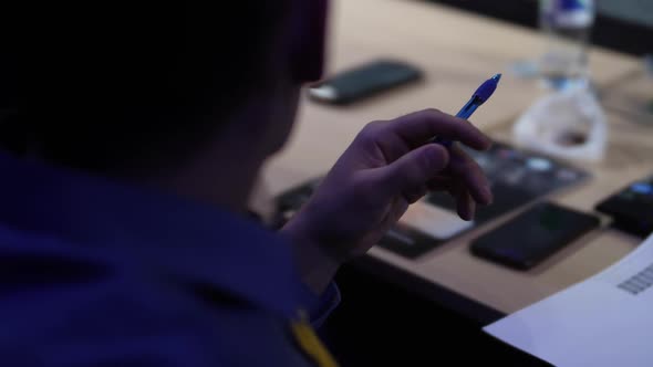 A Man in a Blue Shirt Holds a Pen Against the Background of a Desk alt