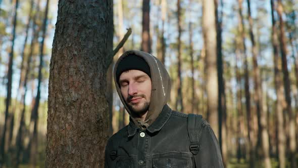 a Man Stands Near a Tree in the Forest and Smiles at the Camera alt