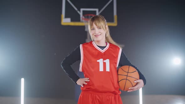 Portrait of a Cheerful Sporty Female Basketball Player Holding a Ball in Her Hands and Looking at alt