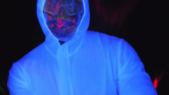 A Man in a White Luminous Suit and Mask Dances in the Dark Under the Neon Light alt