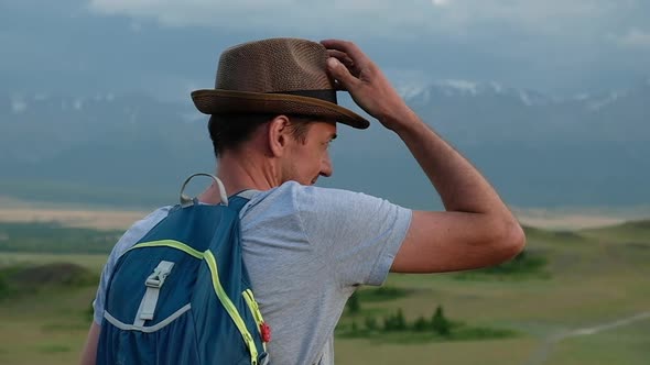 Adult traveler walks through hills of mountain valley with a backpack. Rear view