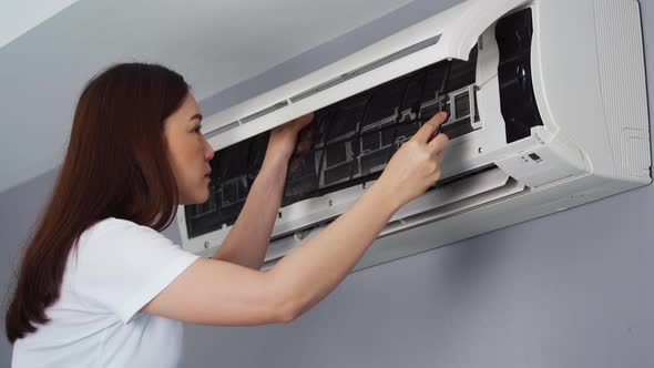 young woman placing back clean filter into air conditioner