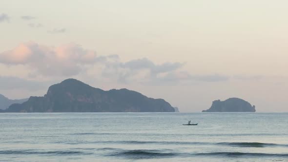 Slow motion shot of paddling man in boat in front of limestone cliffs at dusk seen from beach alt