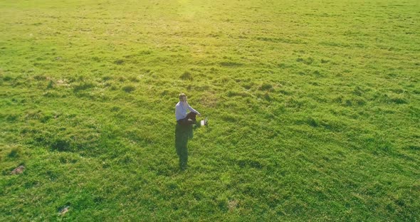 Low Orbital Flight Around Man on Green Grass with Notebook Pad at Yellow Rural Field alt