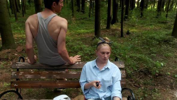 A Girl in a Blue Shirt Explains Something to a Guy in the Woods