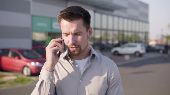 A Young Caucasian Man Talks on a Smartphone in an Urban Area alt